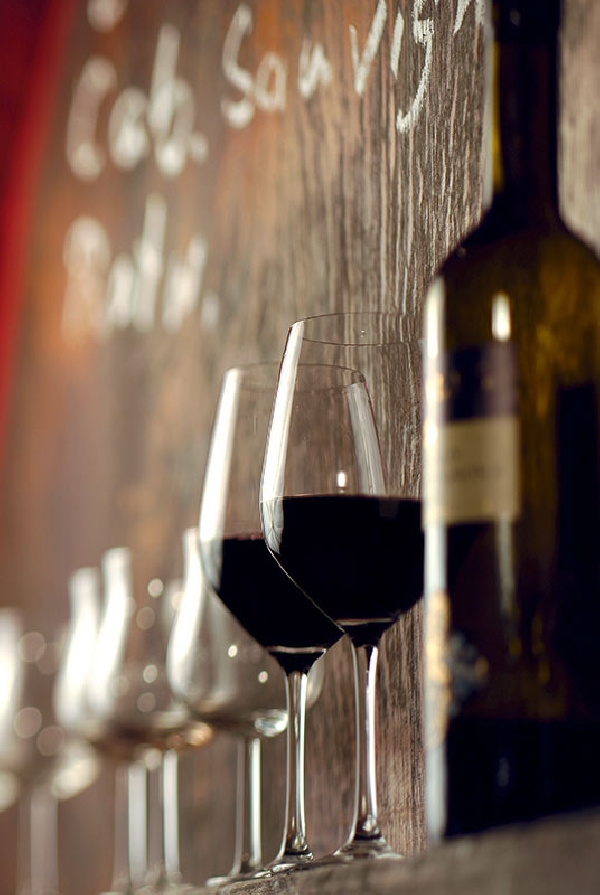 Das Foto zeigt eine Flasche Rotwein und eine Reihe Gläser, von denen zwei gefüllt sind.